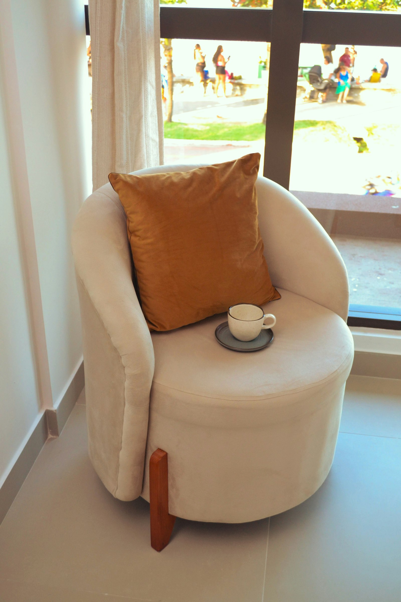 Cream armchair with a cushion and a cup of tea by a sunny window